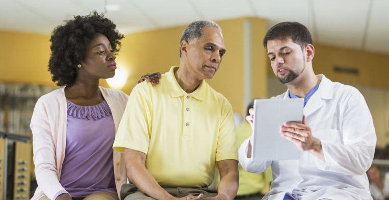 Woman with dark skin tone and male with medium skin tone listening to health care provider.