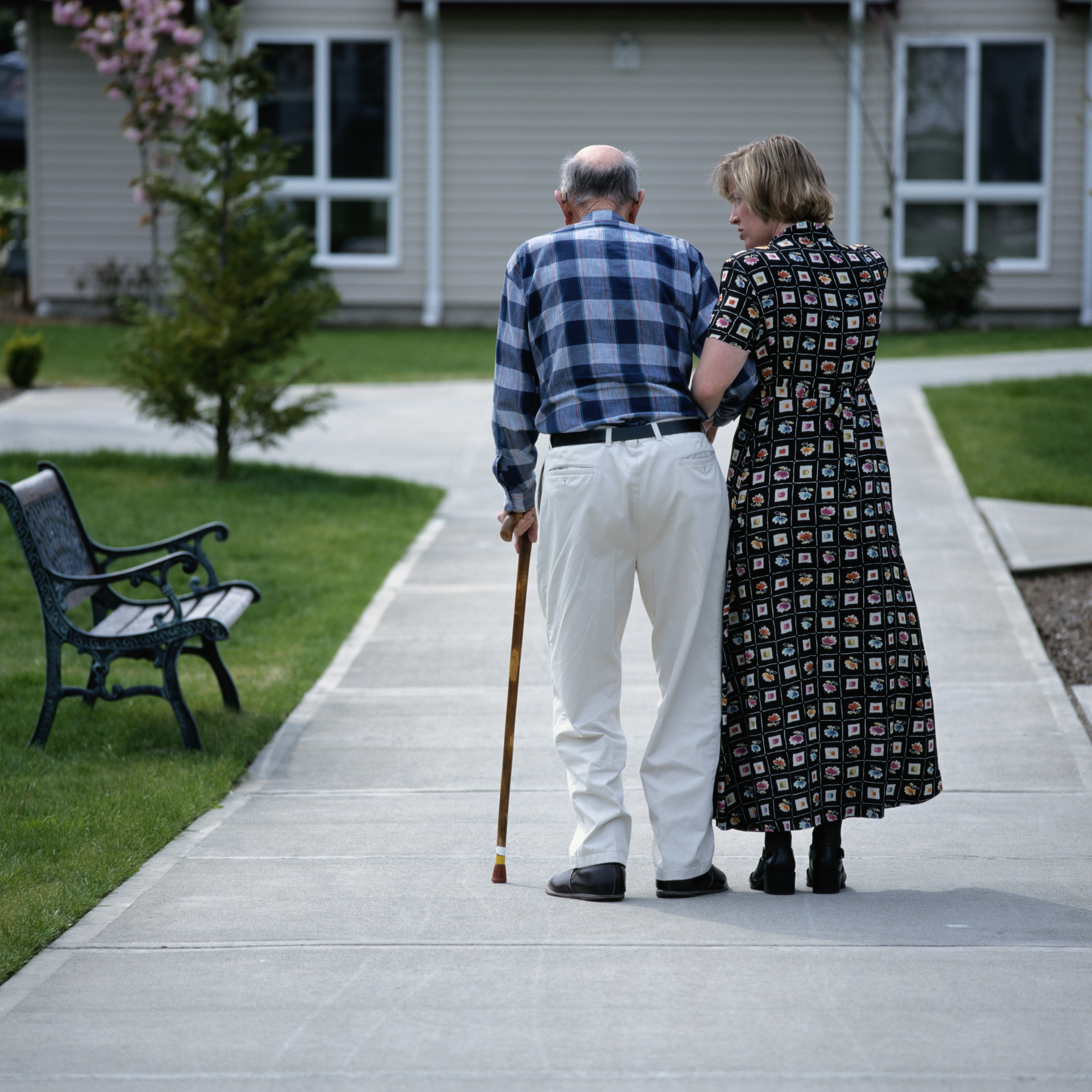 Elderly patient walking with cane and caregiver.