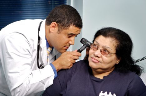 Male health care provider with medium-light skin tone examining the ear of patient with medium-light skin tone.