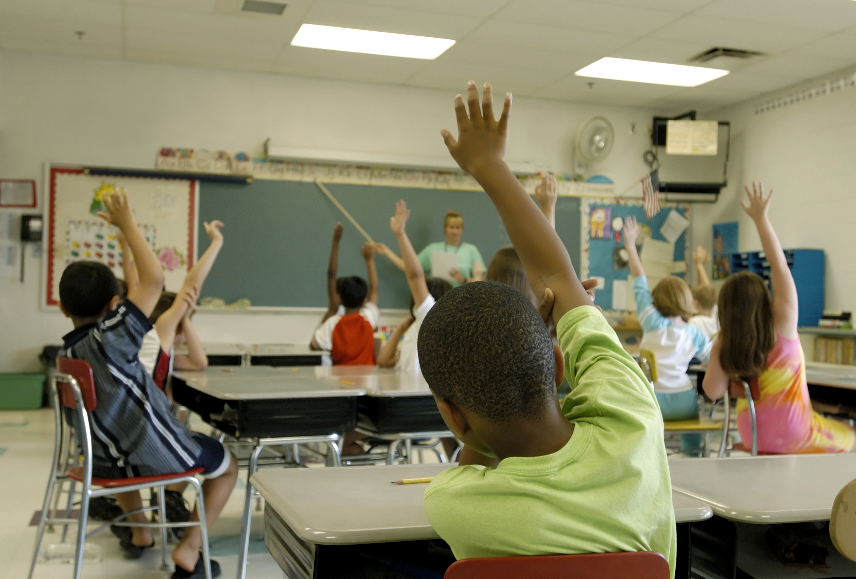 Children raise their hands in the classroom.
