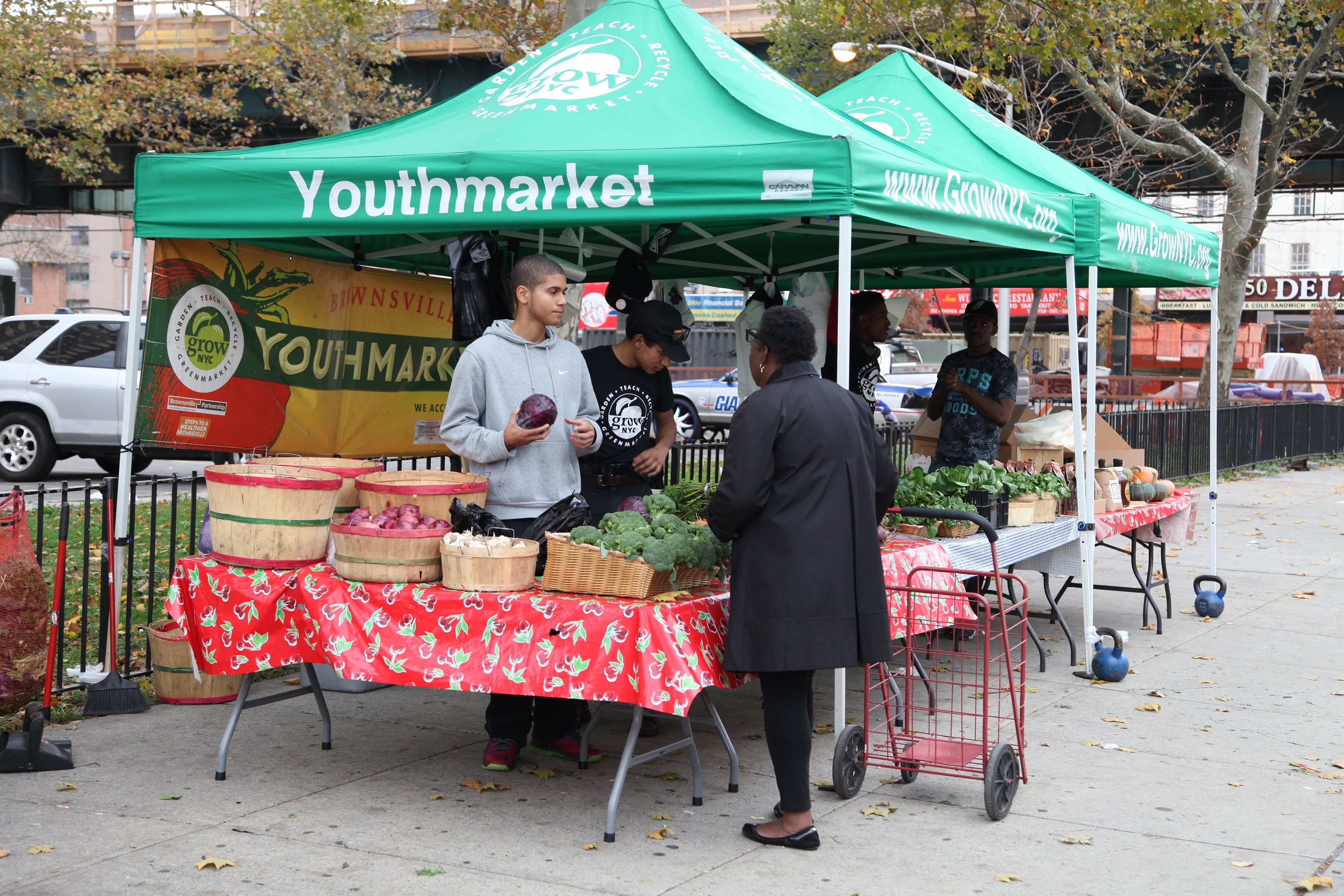 Residents buying healthy food at outdoor food stands that have fruits and leafy, green vegetables.