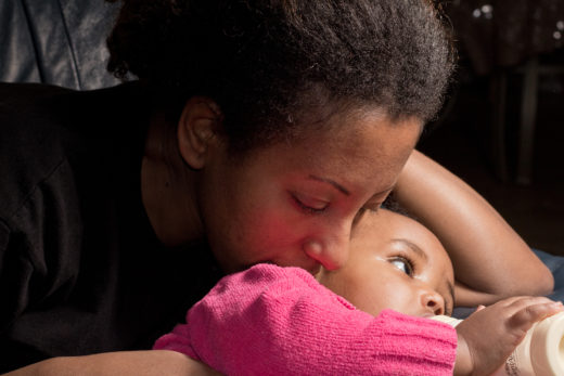 Woman with medium-dark skin tone holds her baby.