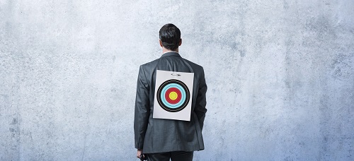 The back side of a man in a suit with a bullseye tacked onto his back.