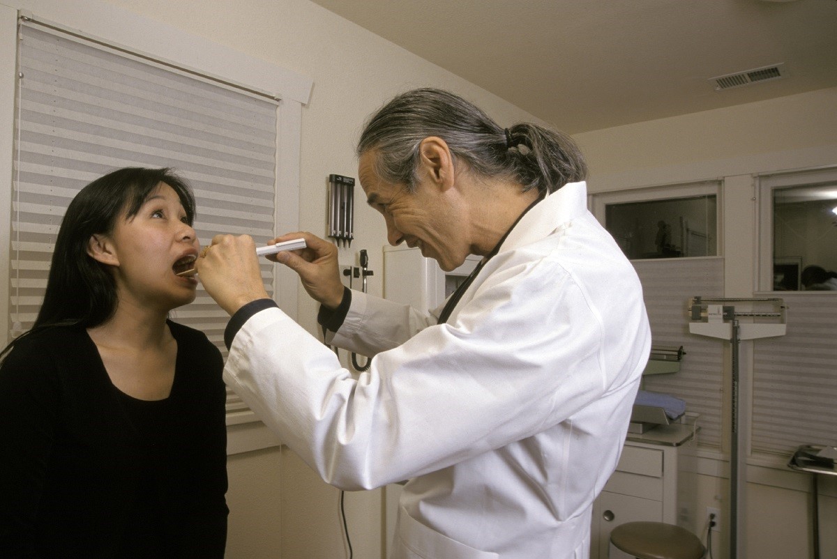A male health care provider examines the tonsils of a female patient.