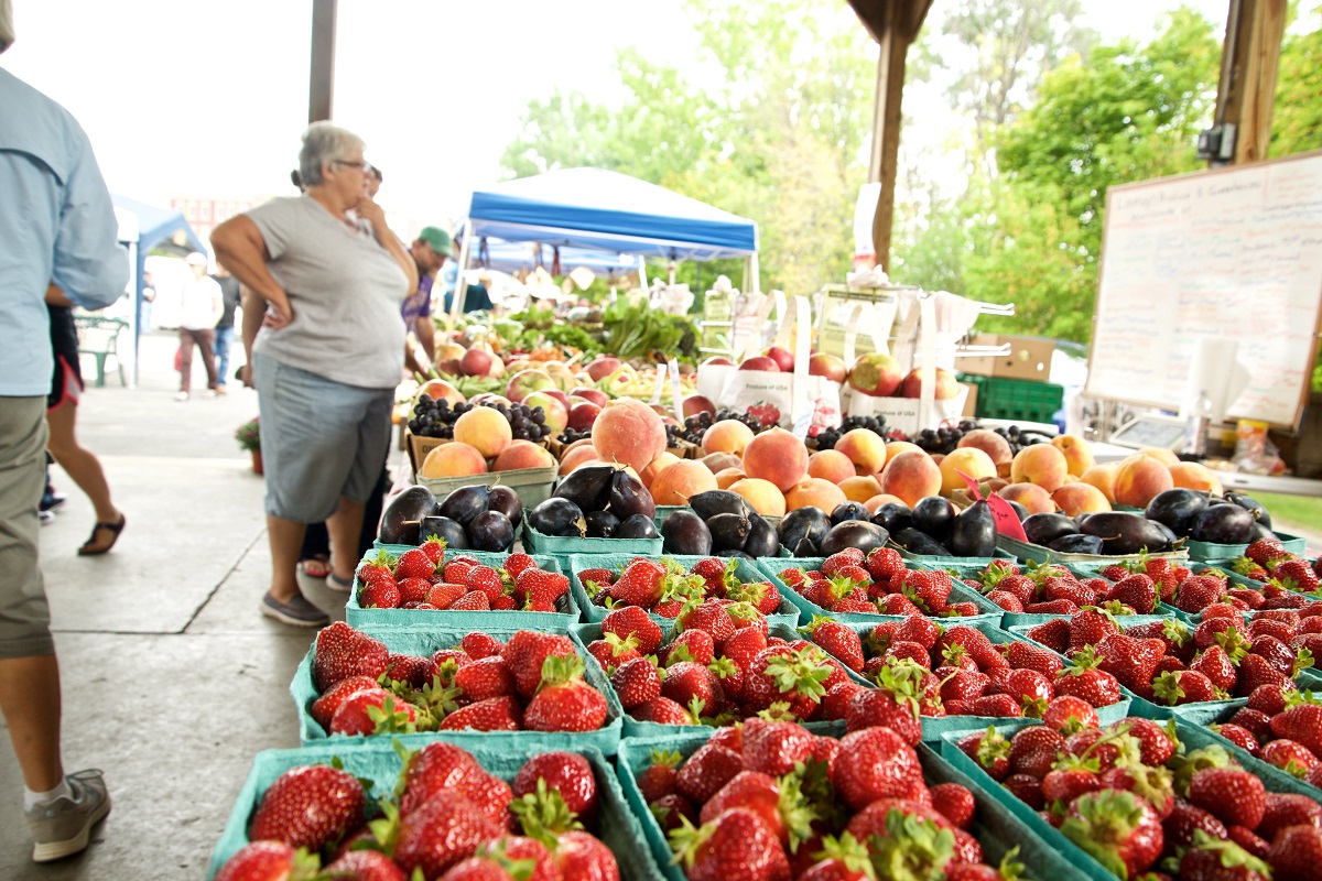 Strawberries, plums, peaches, grapes, and other fruits at a fruit stand in a farmers market.