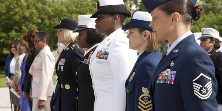 A row a female veterans of various skin tones stands at attention in various veteran uniforms.