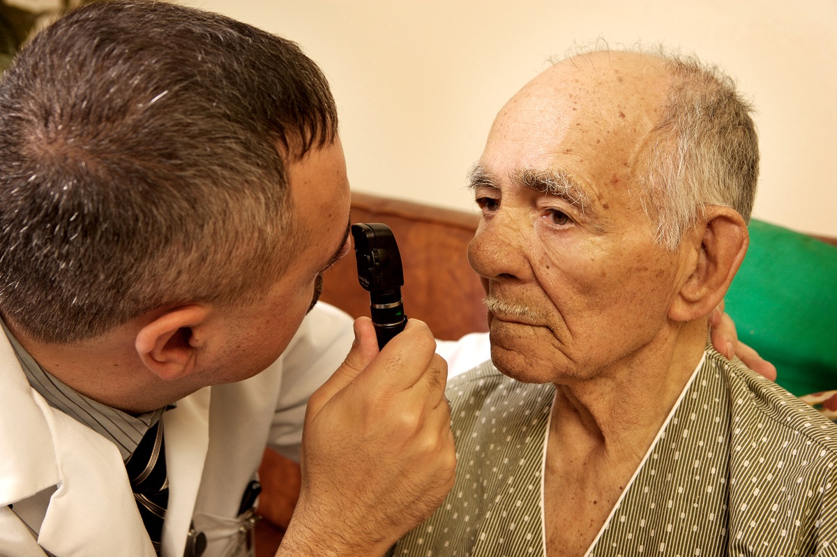 A doctor performs an eye exam on an elderly patient at home.