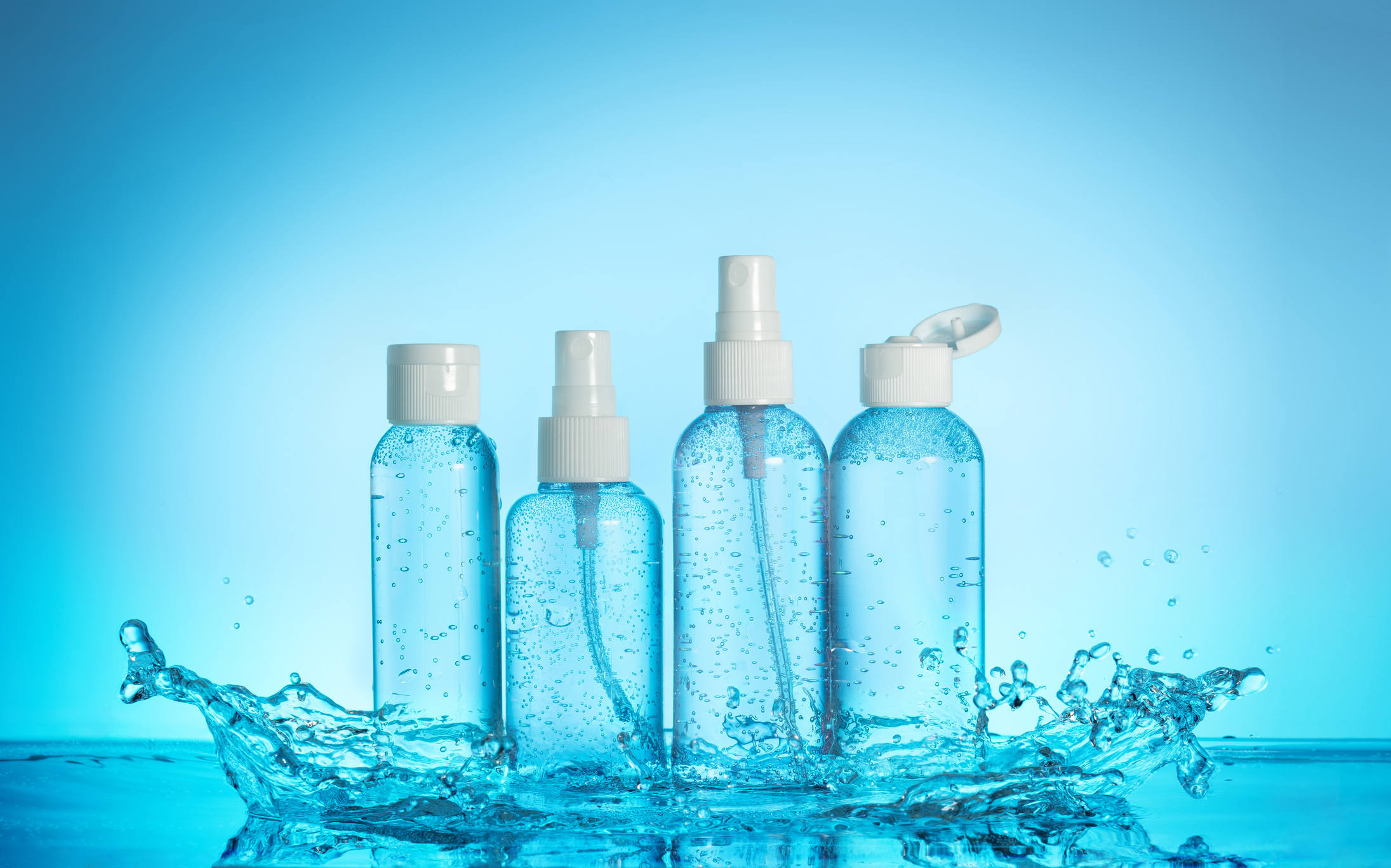 A set of four toiletry bottles sitting on a splash of blue water.