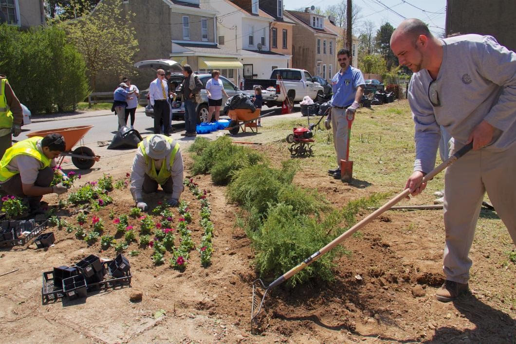 Community members plant flowers and rake soil in an urban community garden.