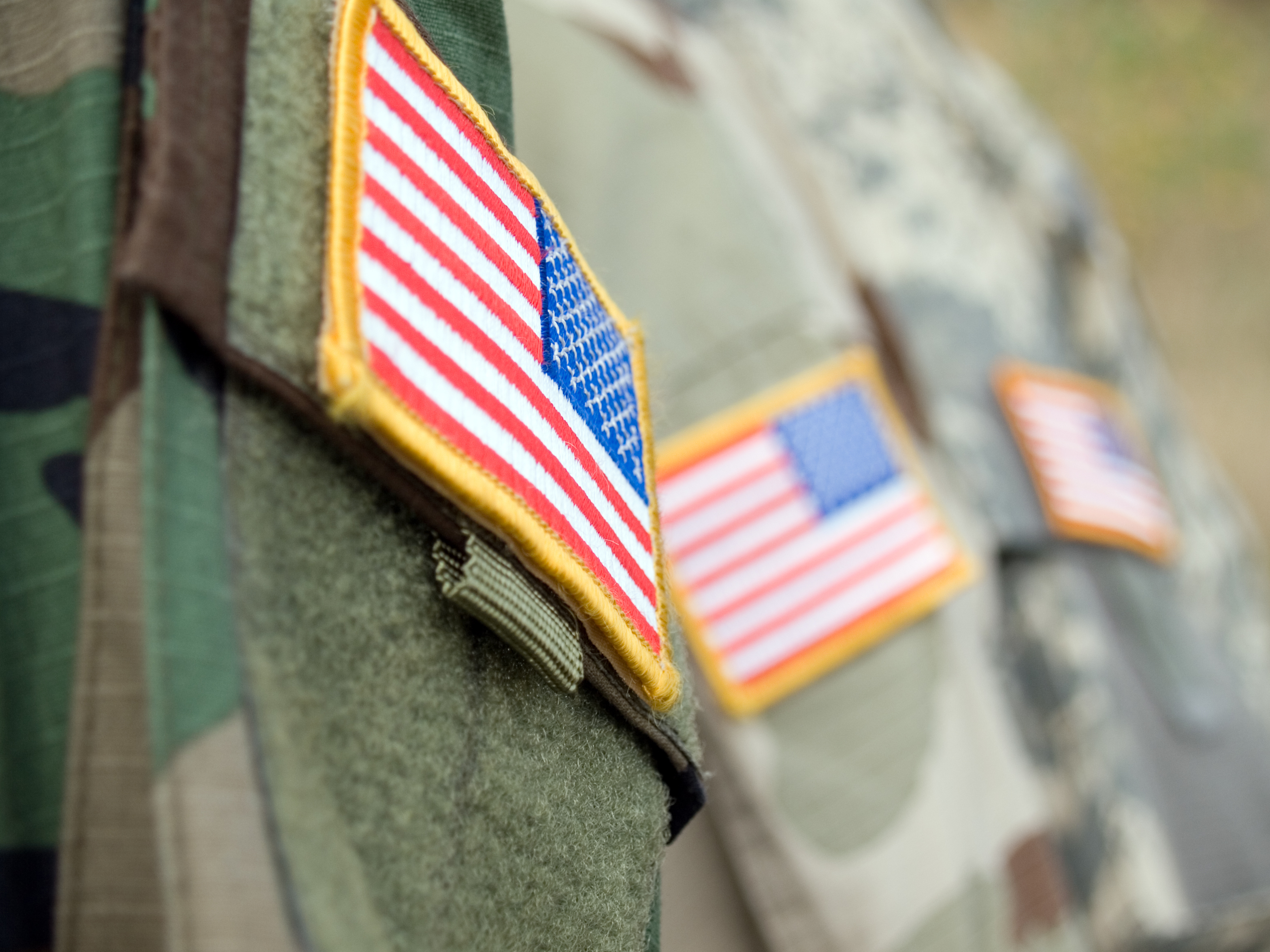 Close-up of American flag patches on the sleeves of three military uniforms.