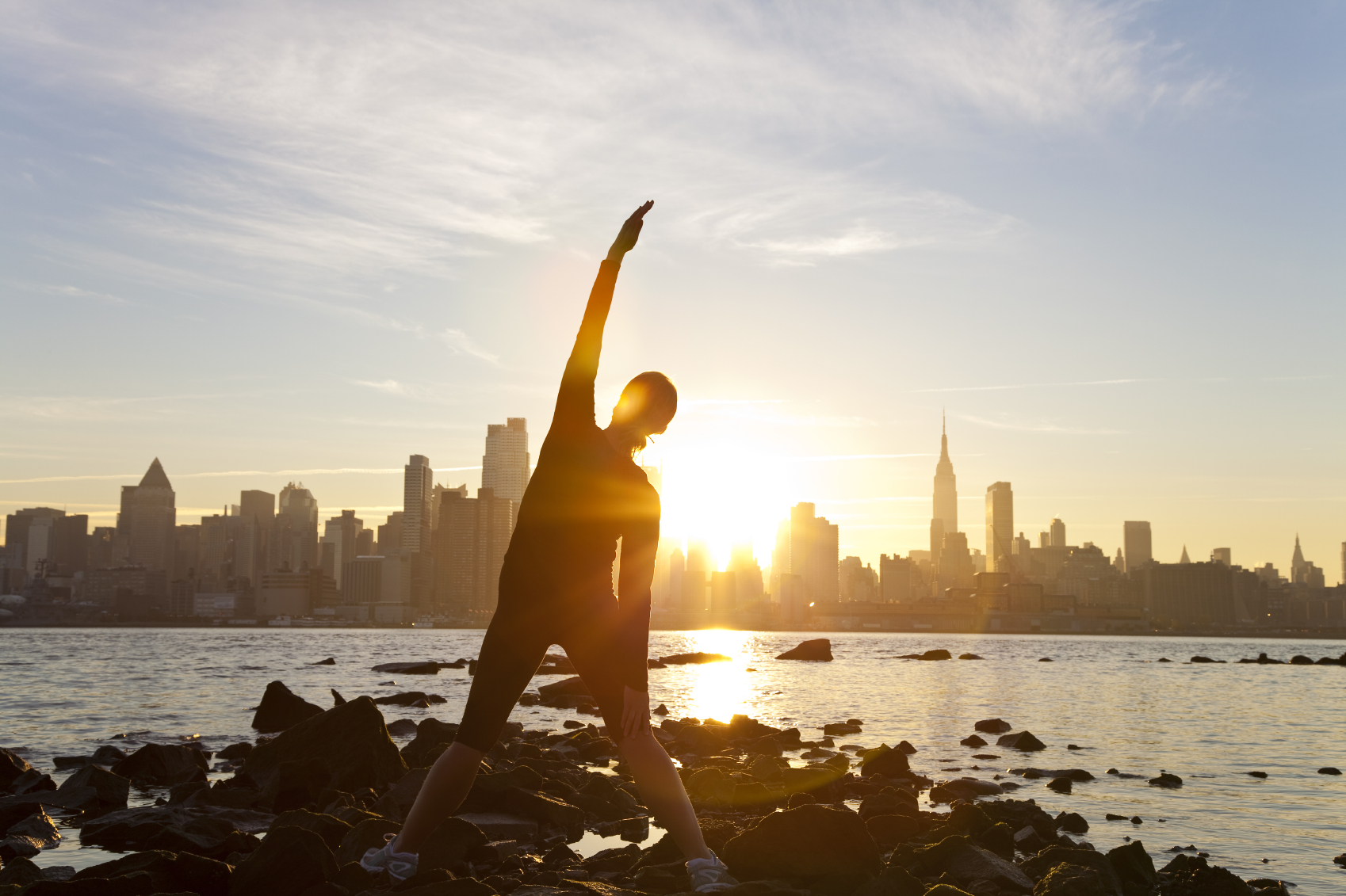 Woman exercising with NYC skyline and sunset in the background.