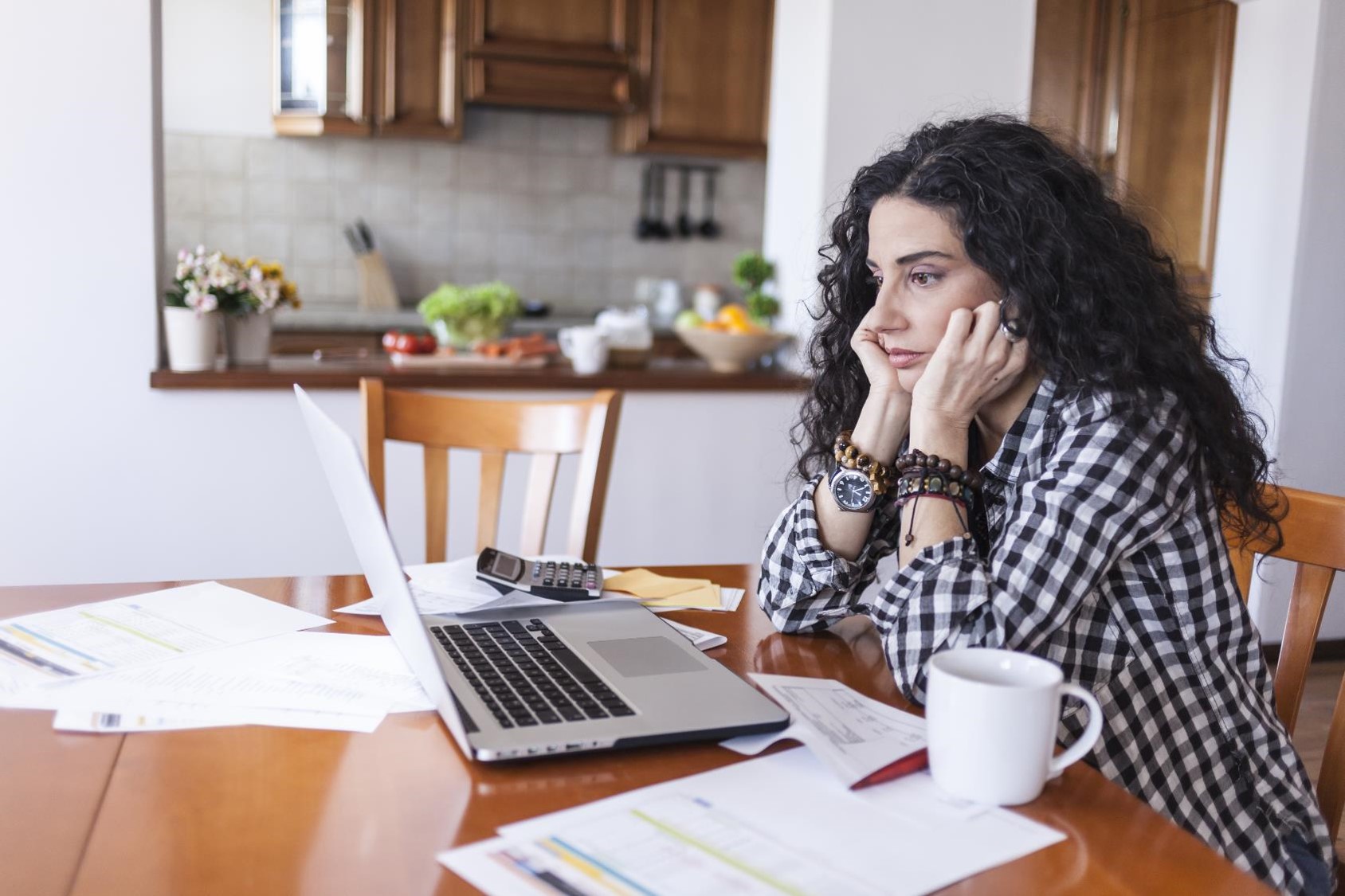 Woman looks at laptop and bills on the table.