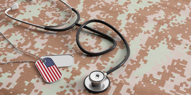 A stethoscope next to dog tags showing an American flag pattern on top of military fatigue print background.