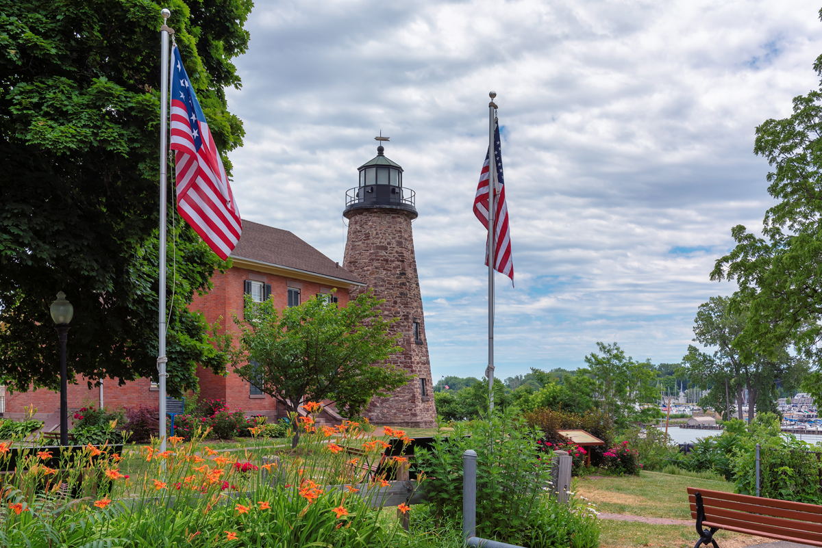 Charlotte Genesee Lighthouse in Rochester, NY, with two American flags in front.