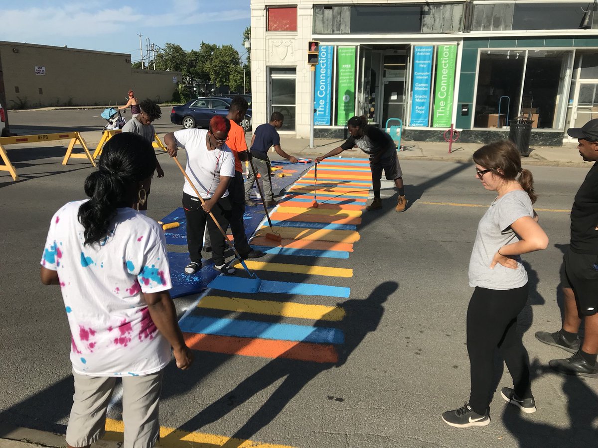 Community volunteers of light and dark skin tone help paint a colorful crosswalk in the North End neighborhood of Niagara Falls.