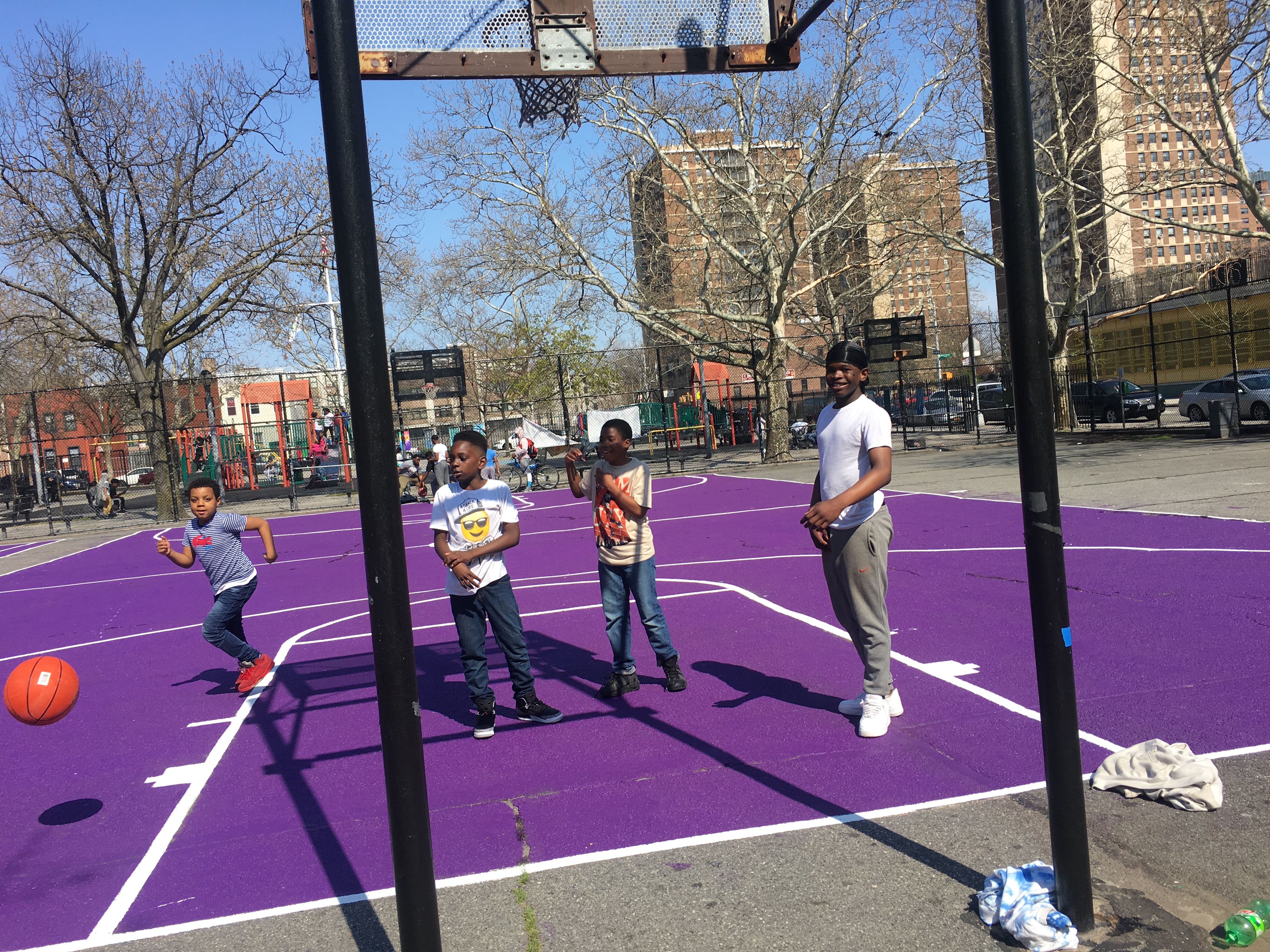 Four young boys with dark skin tone play basketball on a brightly-painted basketball court in New York City.