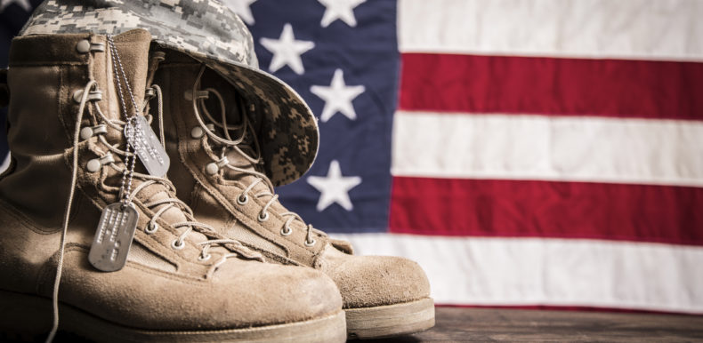 Military boots, hat, and dog tags in front of an American flag.
