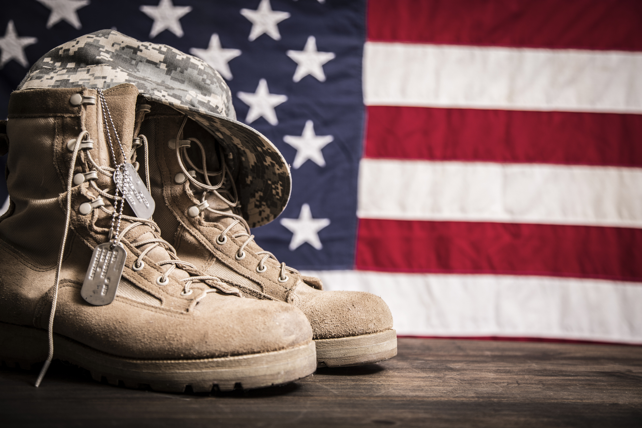 Military boots, hat, and dog tags in front of an American flag.