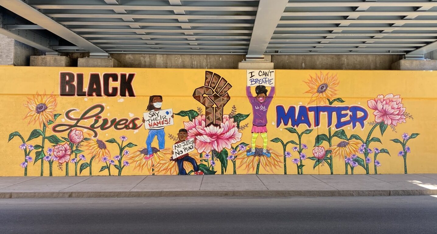Black Lives Matter mural featuring protestors standing among colorful flowers and a raised Black fist in the center.
