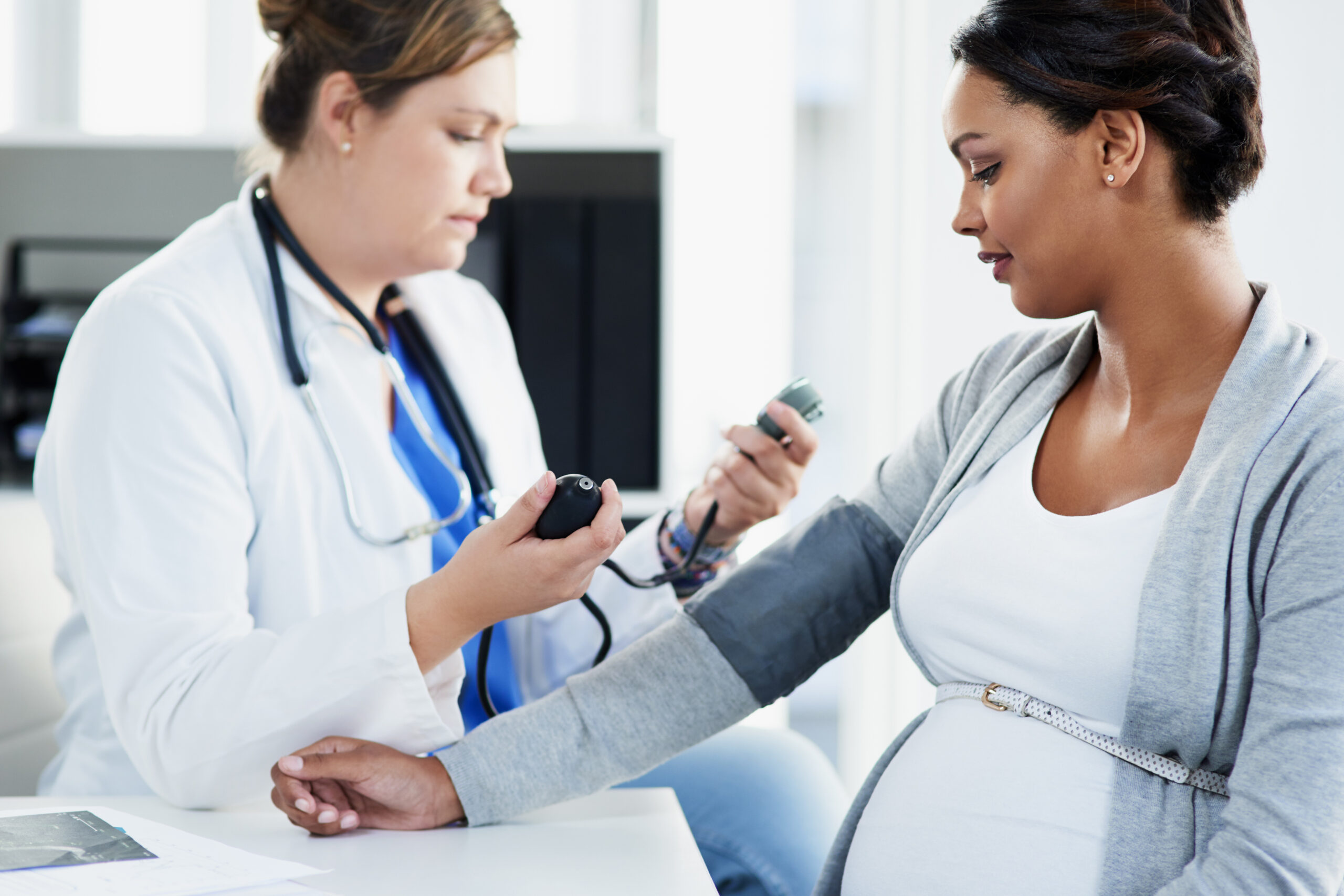 A pregnant woman with a darker skin tone gets her blood pressure checked by a health care provider with medium skin tone.