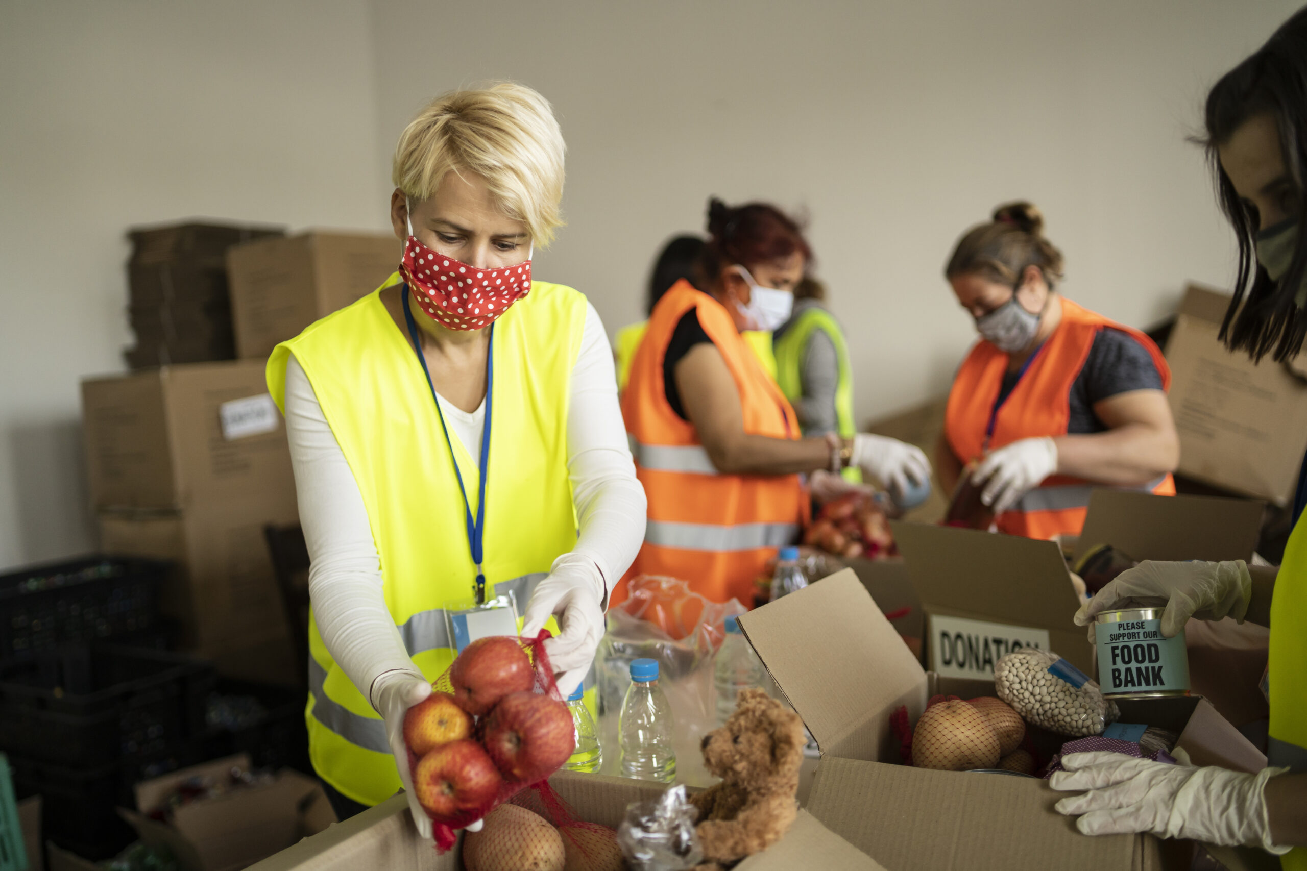 Woman with light skin tone wearing a protective face mask helping to collect food for donation boxes.