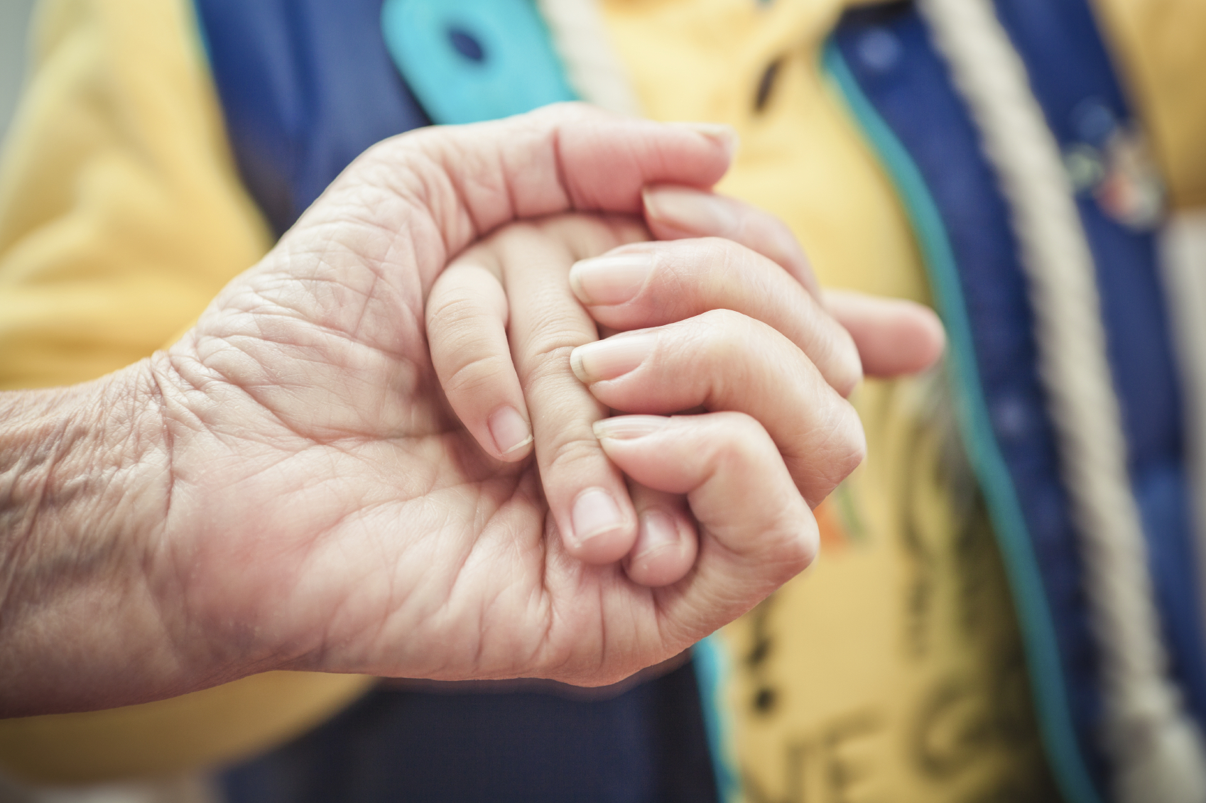 An older person's hand grasps a younger person's hand.