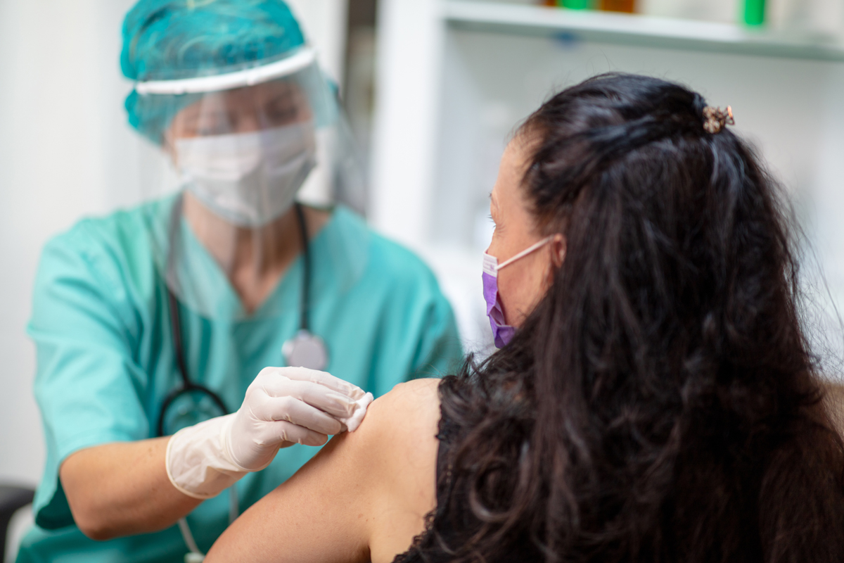 Woman of medium skin tone prepares to get a vaccine by a health care provider with medium skin tone.