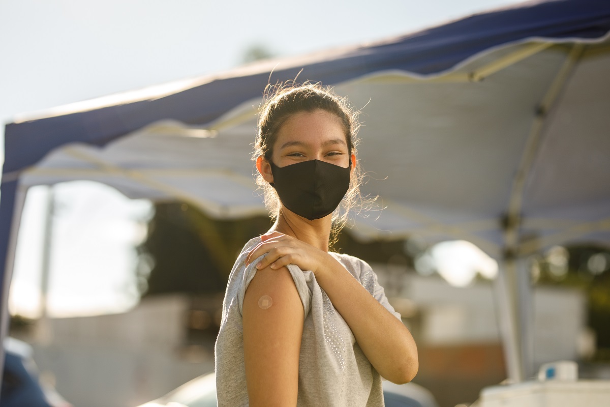 Young adolescent wearing a mask and showing a bandaid on the arm where she's been vaccinated.