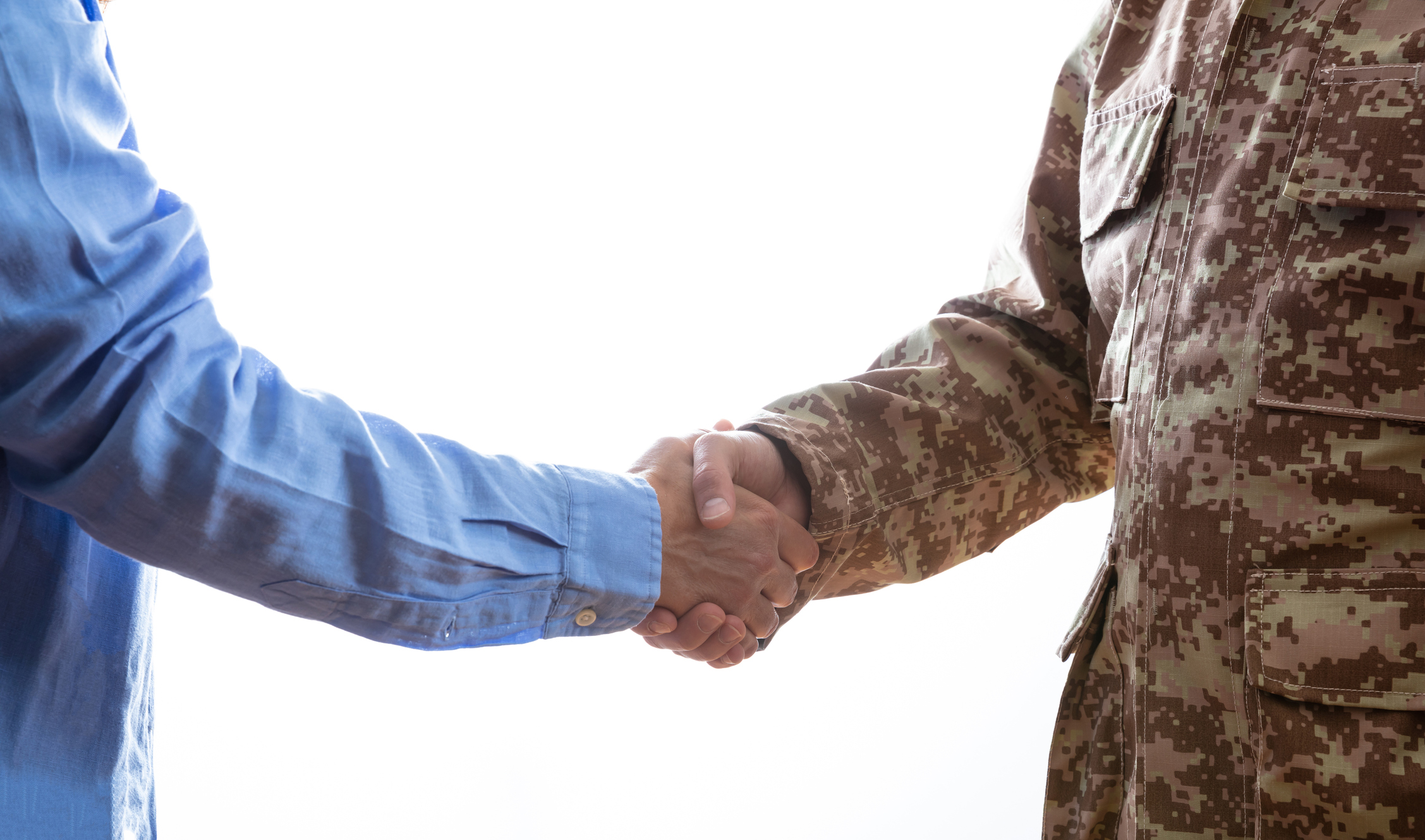 A close-up image of a handshake between a veteran wearing military fatigues and a civilian wearing a light blue button-down shirt.