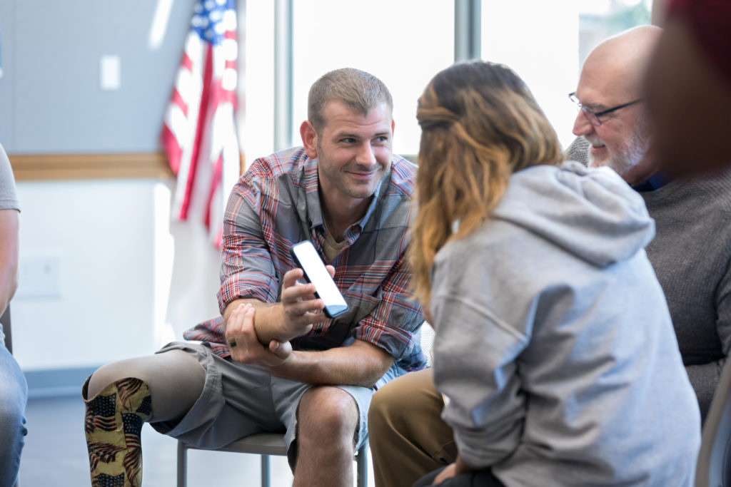 Veteran with an artificial leg shows his smartphone to other members in his support group. 