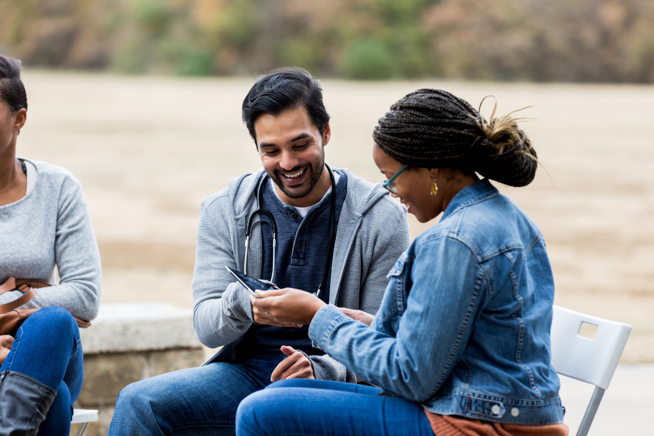 Two people, one with a stethoscope, sit close together looking at a digital tablet and smiling.