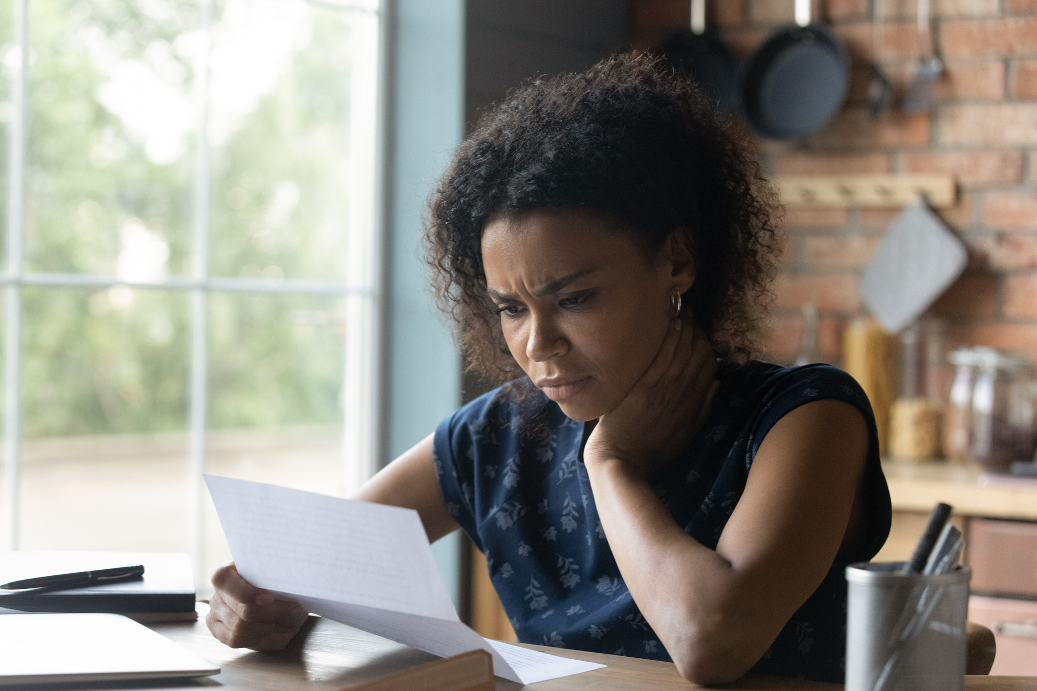 A woman with medium-dark skin tone looking distressed as she examines her bills