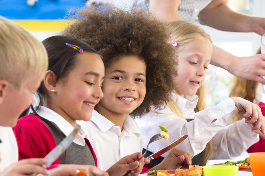 Child with medium-dark skin tones eating in a school cafeteria. 