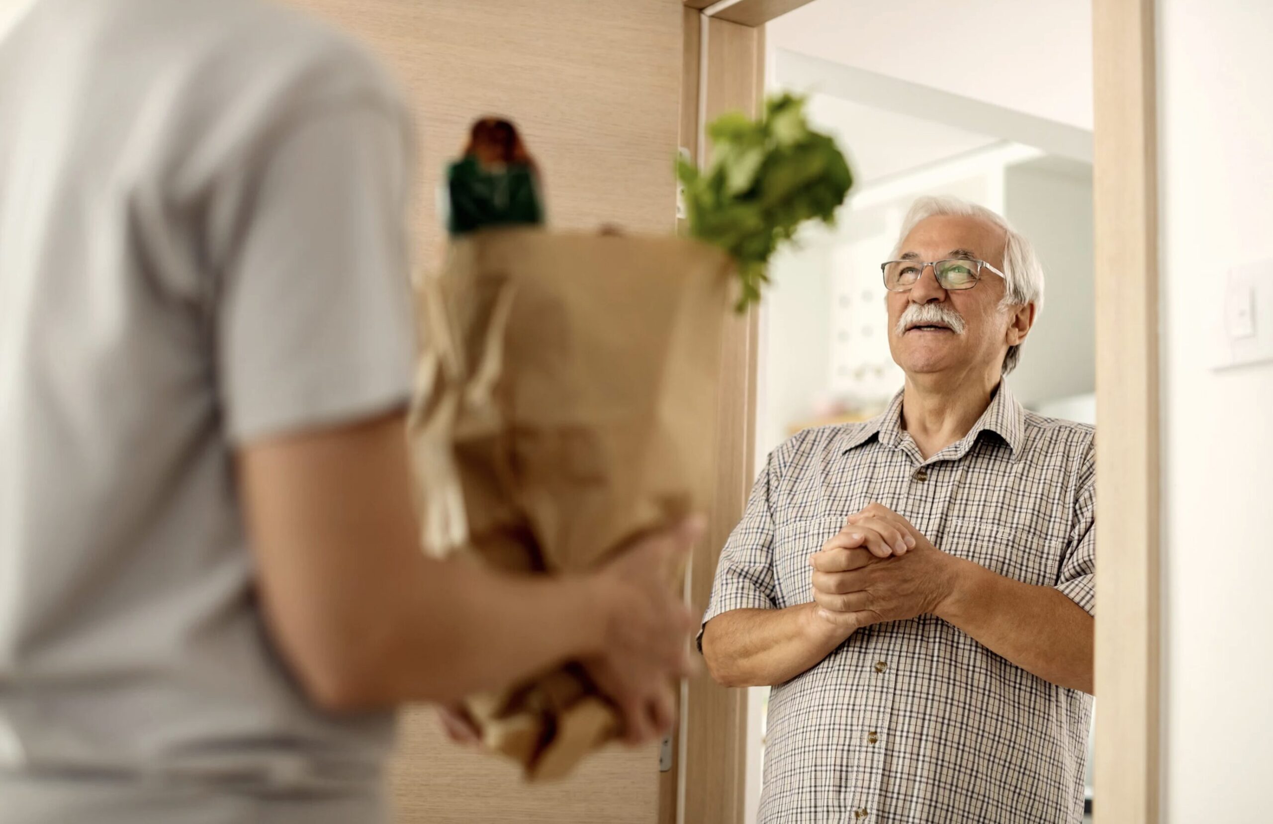 Older adult man talking to a courier while receiving groceries delivery at home.